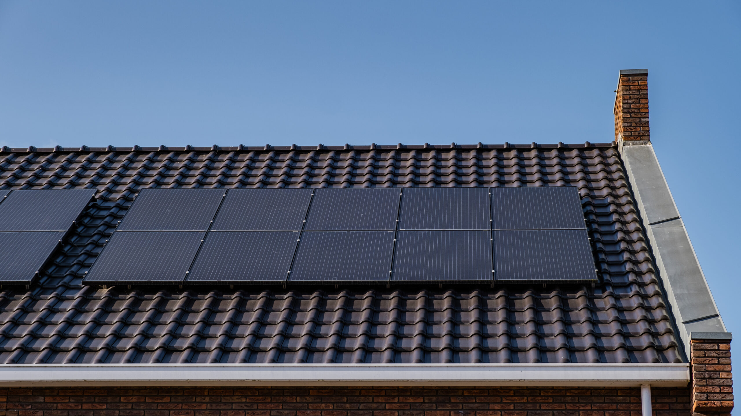 Newly build houses with solar panels attached on the roof against a sunny sky Close up of new building with black solar panels. Zonnepanelen, Zonne energie, Translation: Solar panel, , Sun Energy